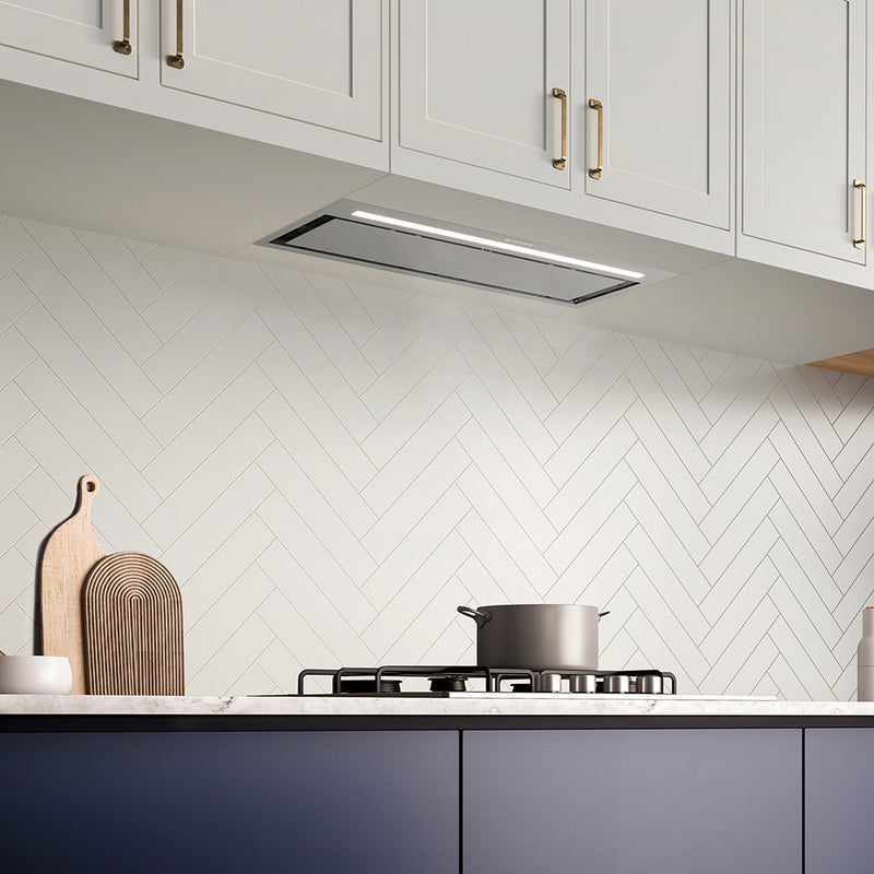 faber inca lux plus lifestyle stainless steel insert kitchen range hood with hidden controls, led light bar, and perimeter aspiration in modern kitchen. white upper cabinets, navy lower cabinets and white herringbone backsplash