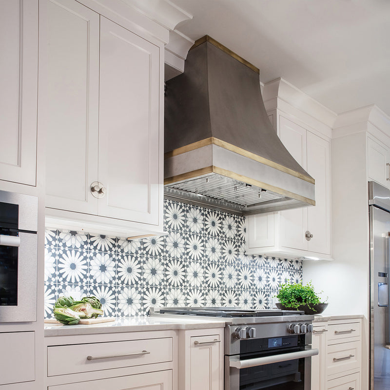 faber inca pro plus iindustrial stainless steel kitchen insert range hood lifestyle image in a transitional kitchen setting. bold blue and white patterned backsplash and white cabinets.